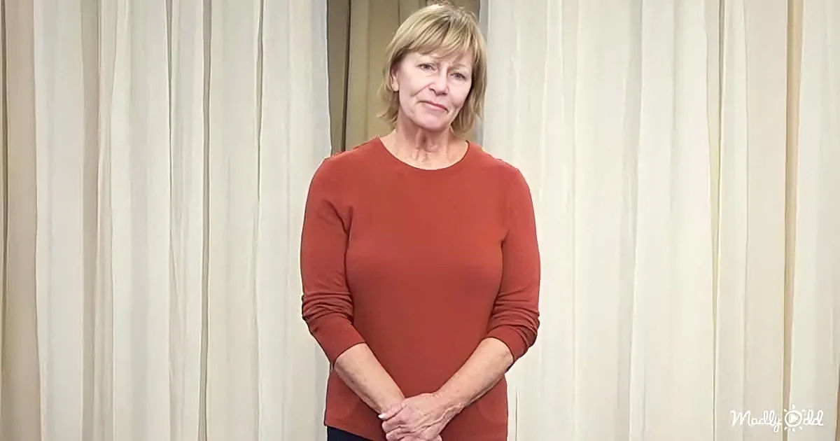 A woman in a red top stands with hands clasped, against a light curtain backdrop.