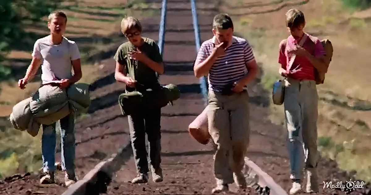 Four individuals walk along a dirt path, each carrying a bag, in a rural setting.