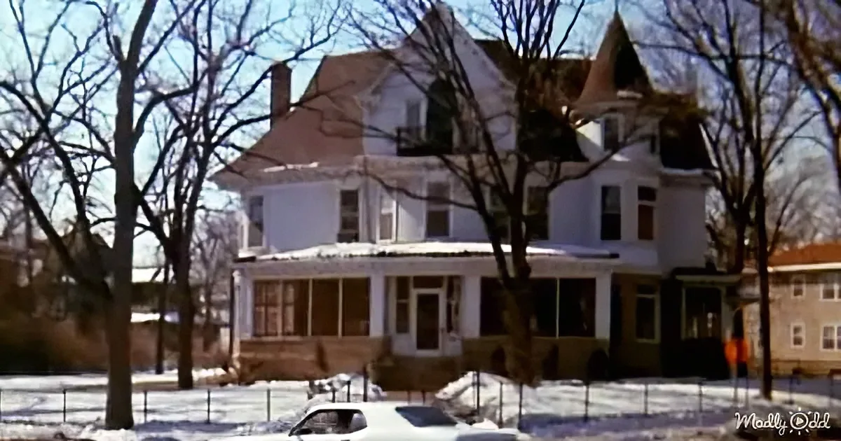 A white Victorian-style house with snow on the ground and bare trees in front.
