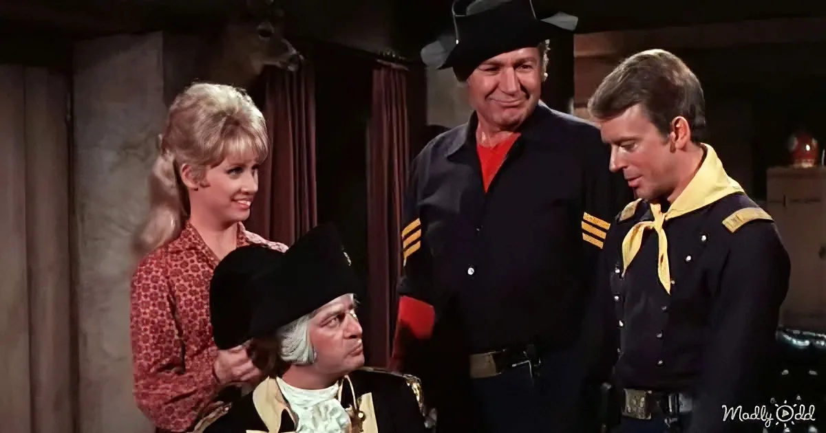 A man in a black uniform with yellow accents stands beside another in a black jacket and red shirt, both looking at a...
