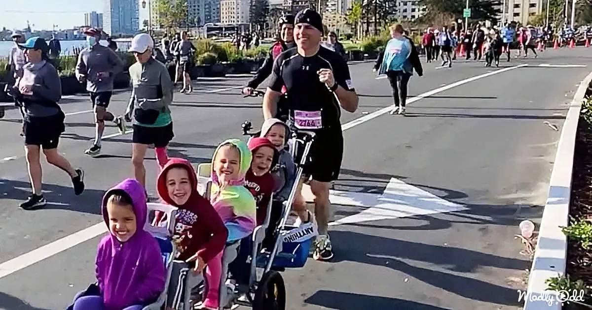 A man pushes a stroller with smiling children while running in a race, surrounded by other runners.