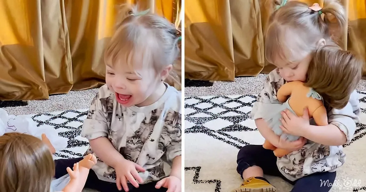 A child with Down syndrome sits on a patterned rug, interacting with a doll and another child nearby.