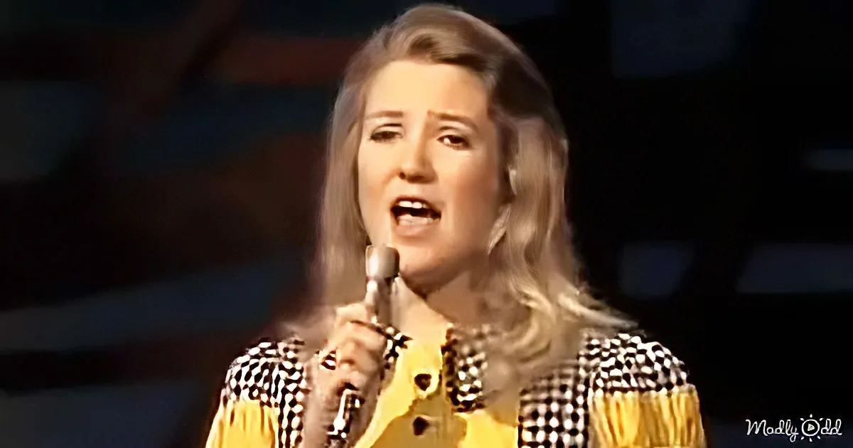 A woman with blonde hair in a checkered dress sings into a microphone.