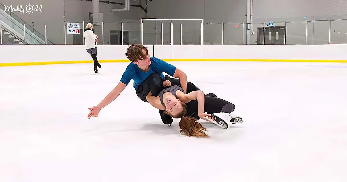 A man and woman are on an ice rink, the woman is lying on the ice with the man supporting her.