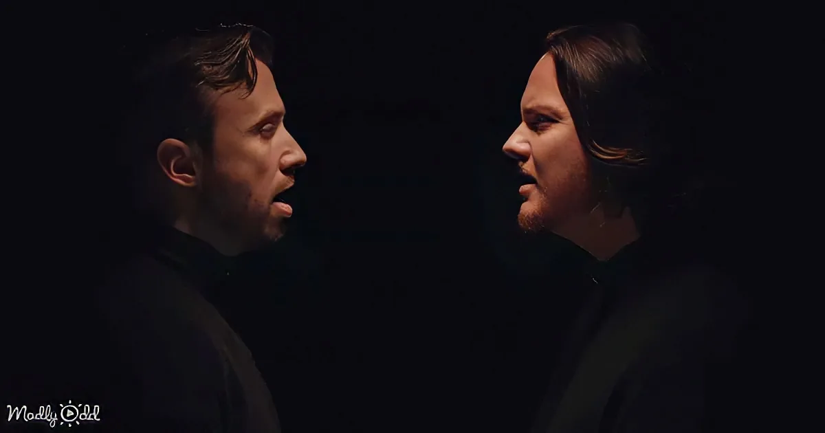Two men face each other against a dark background, one with a beard, both wearing dark clothing.