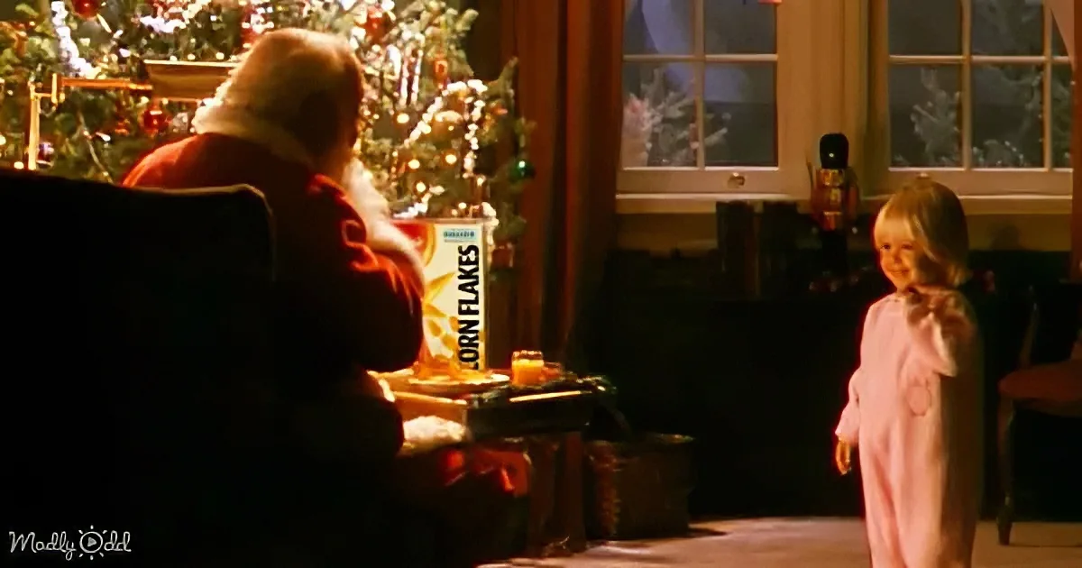 Santa Claus sits by a Christmas tree, eating breakfast, while a child in pajamas looks on.