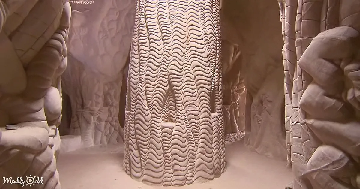 A sand sculpture with intricate wavy patterns stands tall in a cave-like setting.