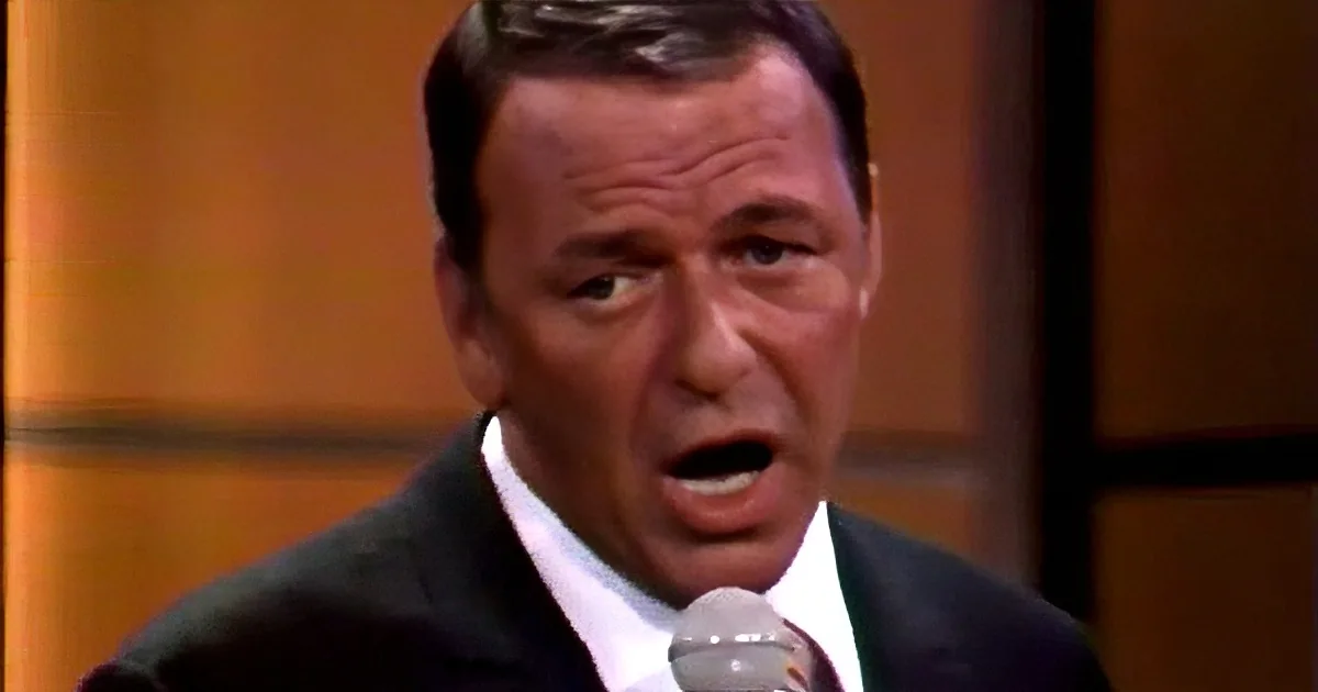 A man in a suit sings into a microphone, his eyes closed, against a warm background.