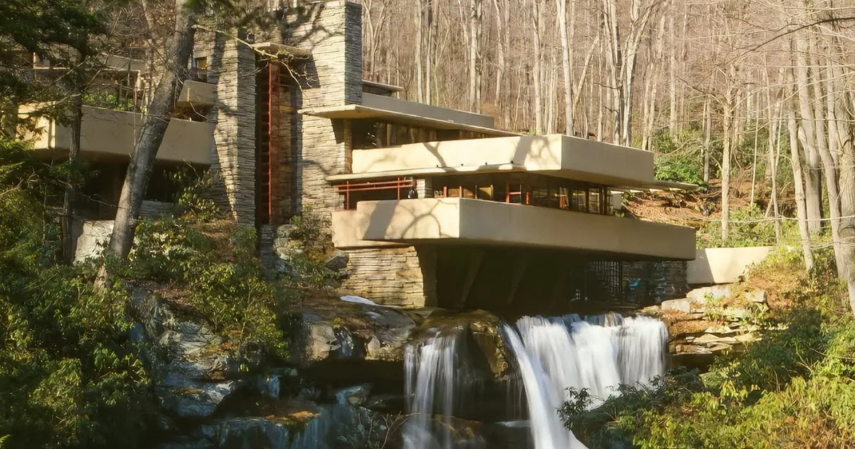 A modernist house with cantilevered balconies overlooks a cascading waterfall in a forested area.