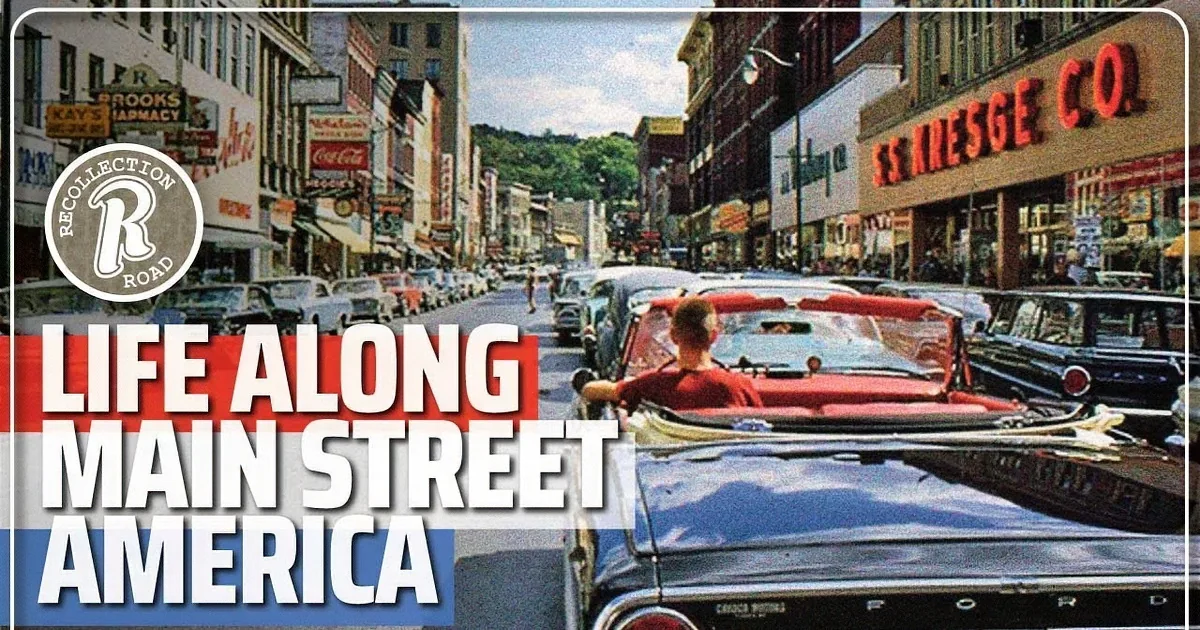 A man drives a red convertible down a bustling street lined with vintage cars and shops.