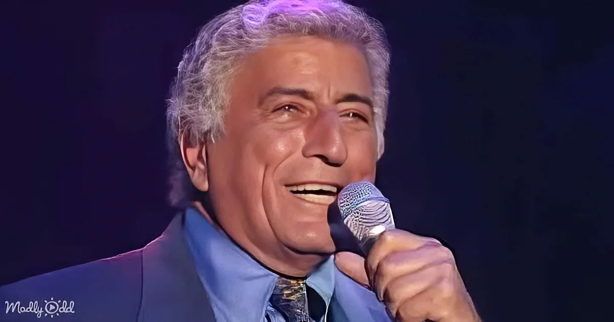 A man with gray hair, wearing a blue suit and tie, sings into a microphone on stage.