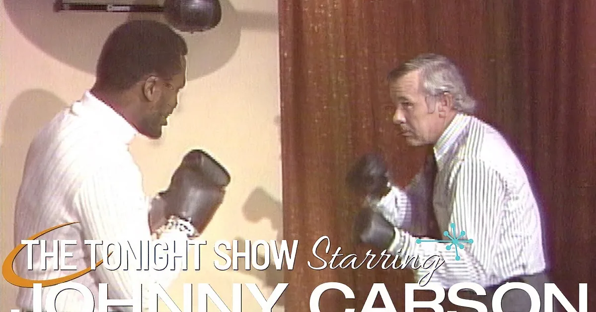 Two men in white shirts and boxing gloves are practicing punches in a room with wooden walls.