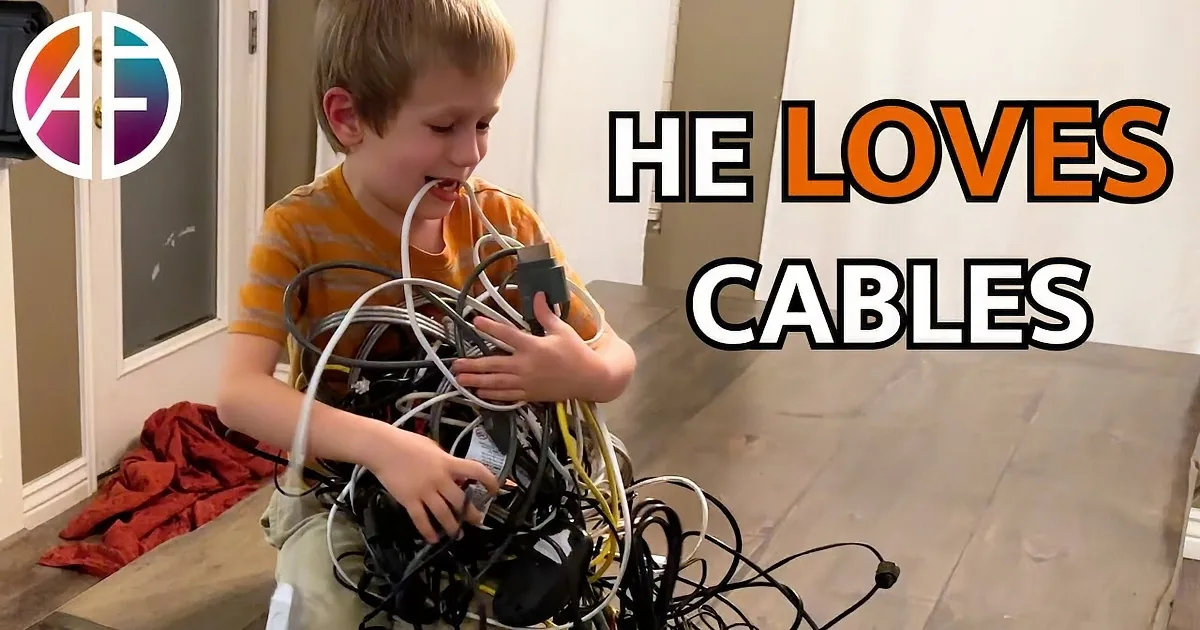 A young boy sits on a bench, holding a tangled pile of cords and electronics.