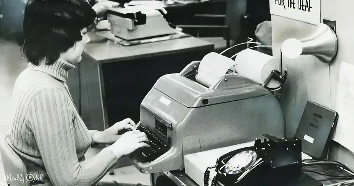 A woman types on a vintage typewriter in a workspace, surrounded by office equipment.