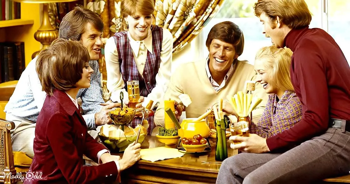 A group of six people, dressed in 1970s attire, are gathered around a table, enjoying food and drinks in a cozy, warmly...