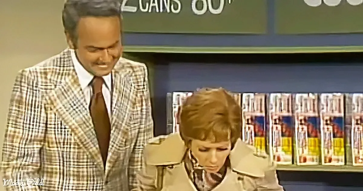 A man in a plaid suit stands beside a woman in a trench coat, both looking down, with a store display of magazines in the...