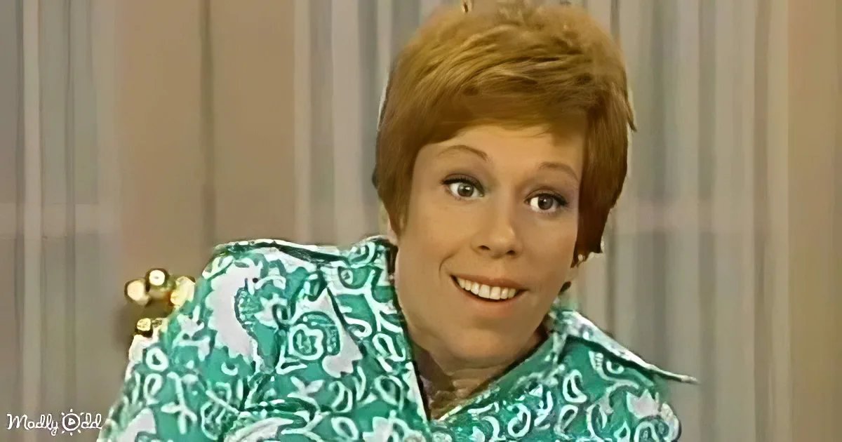 A woman with short red hair, wearing a green patterned shirt, smiles while seated in a chair.