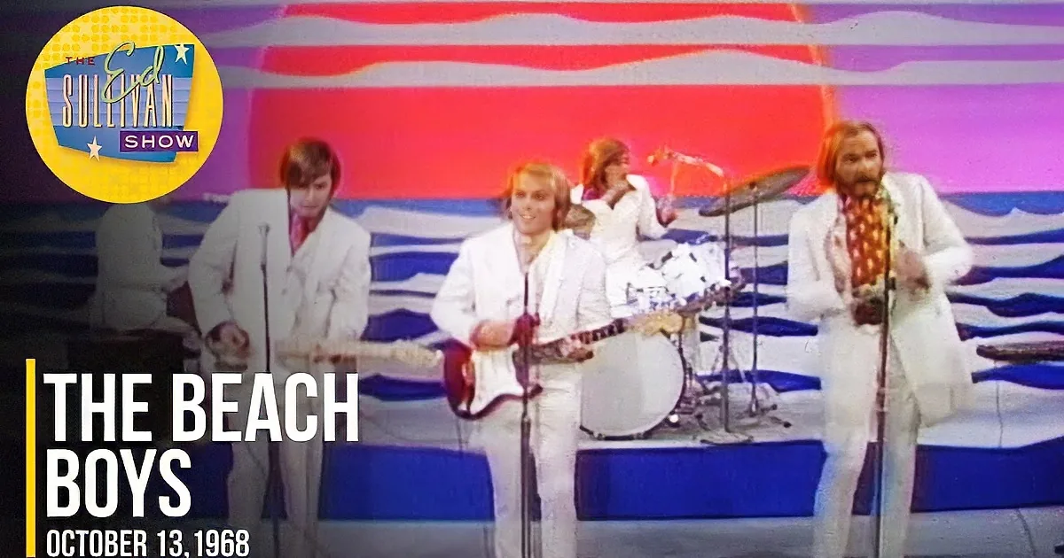 A band in white suits performs on stage with a colorful, abstract background.