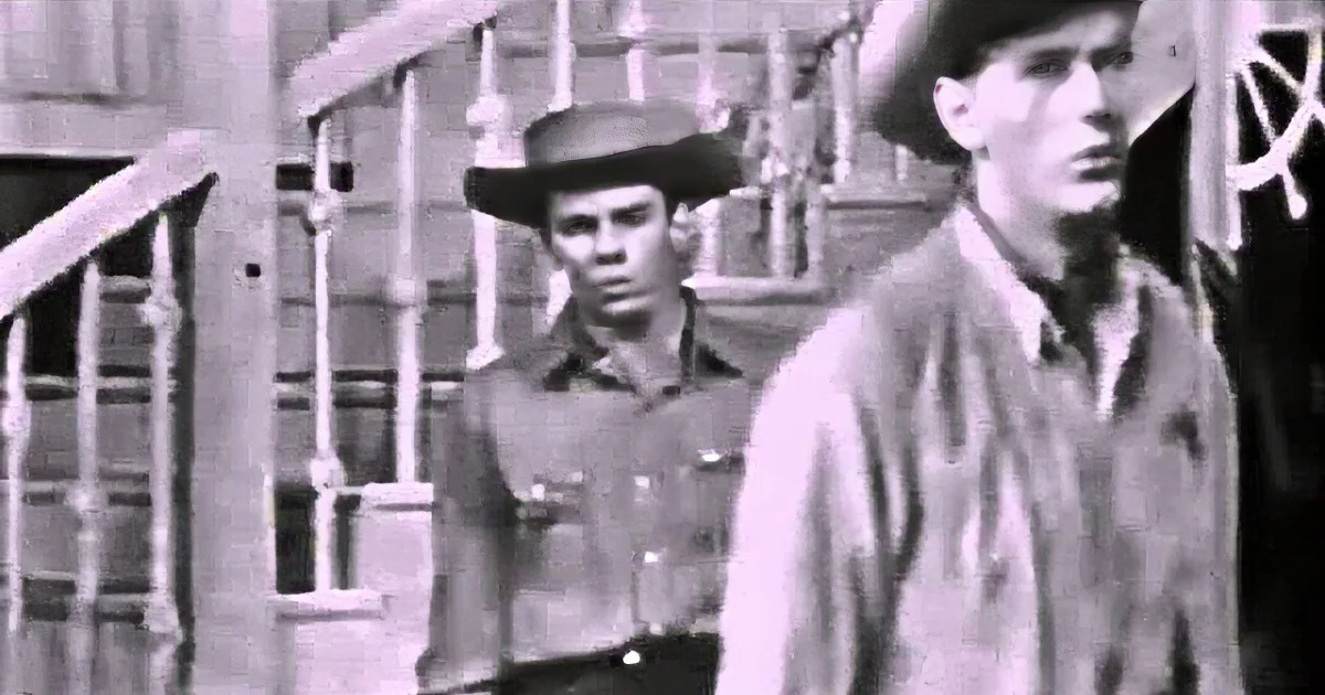 A man in a cowboy hat and shirt stands in a dimly lit room, looking upward with a serious expression.