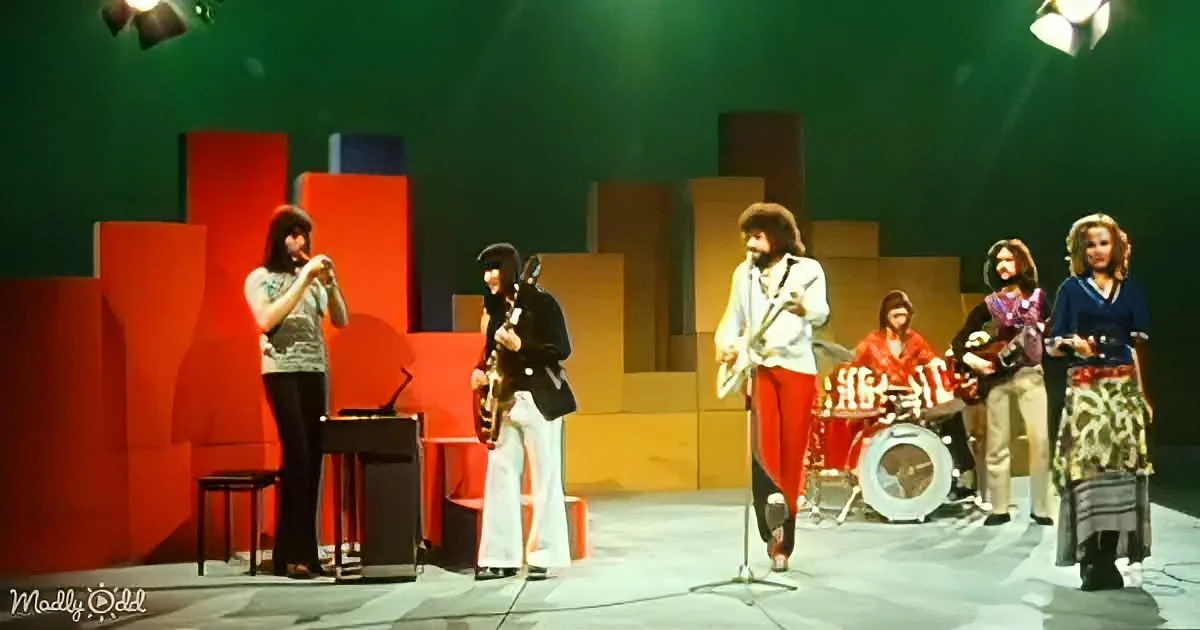 A band performs on stage with colorful geometric backdrop and vintage instruments.