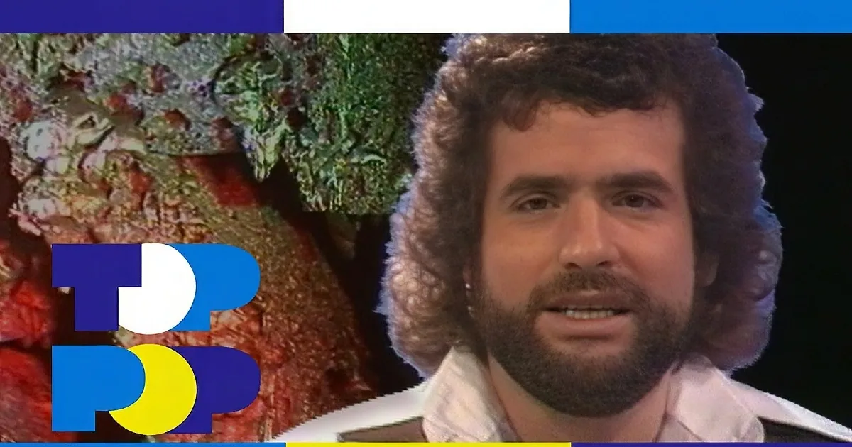 A man with curly hair and a beard sings passionately, eyes closed, against a green background.