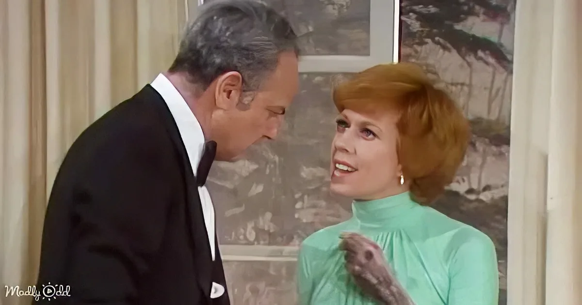 A man in a tuxedo leans towards a woman in a mint green turtleneck, holding a small object.