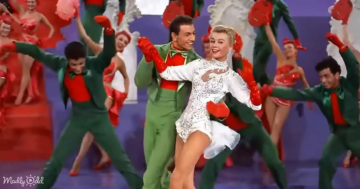 A man and woman in festive costumes dance joyfully, surrounded by a colorful ensemble of performers.