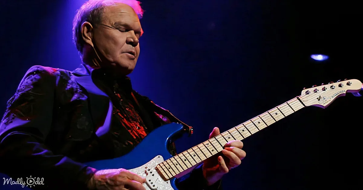 A man plays a blue electric guitar on stage under blue lighting.