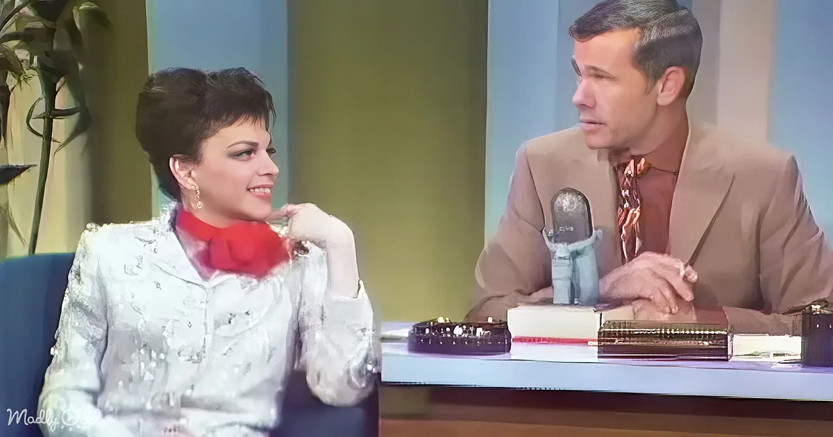 A woman in a white sequined dress smiles at a man in a suit at a desk with a microphone.