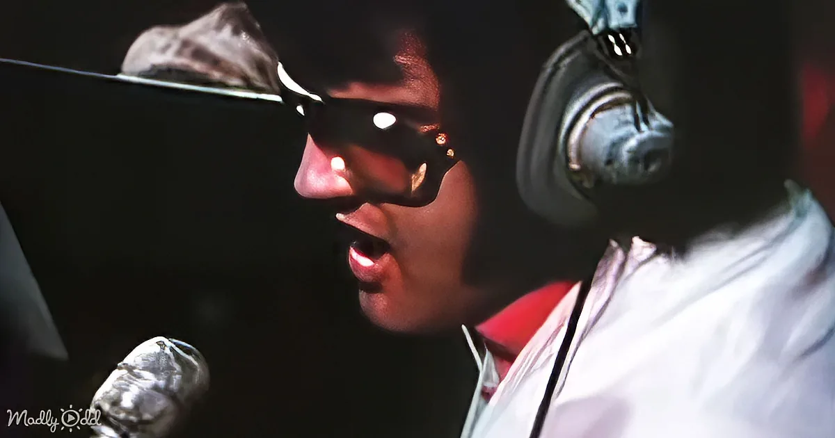 A person wearing sunglasses and headphones is singing into a microphone in a recording studio.