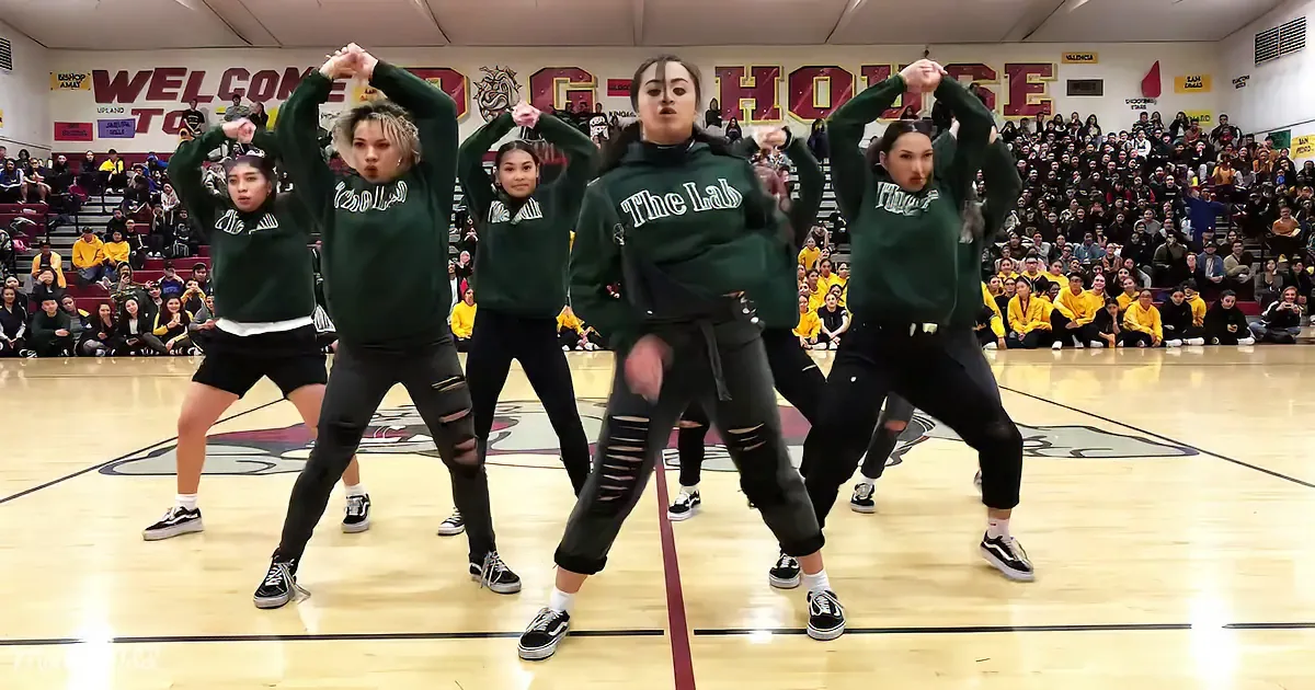 Five dancers in green "The Lab" sweatshirts perform a synchronized routine on a basketball court.