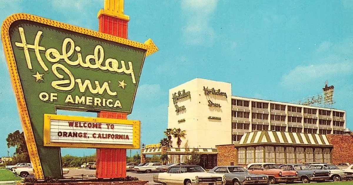 A vintage Holiday Inn of America sign welcomes visitors to Orange, California, with classic cars parked in front.
