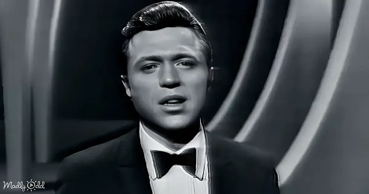 A man in a tuxedo with a bow tie, looking upwards, in a black-and-white setting.