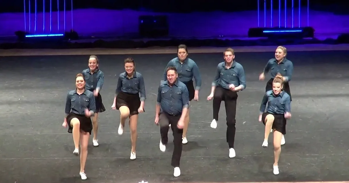 A group of dancers in matching outfits perform a synchronized routine on stage.