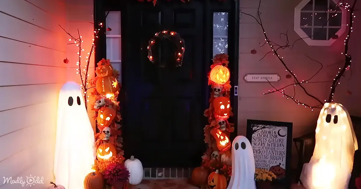 A Halloween-themed front porch with glowing ghost figures, jack-o'-lanterns, and a wreath adorned with lights.