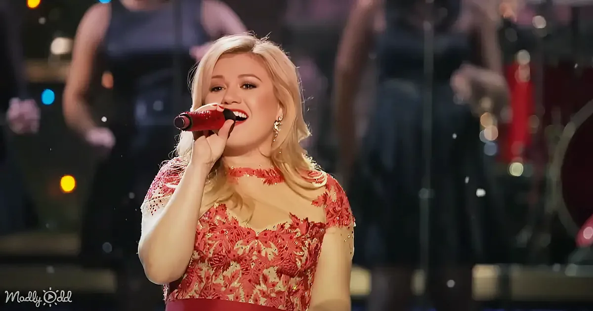A woman in a red floral dress sings into a microphone on stage.