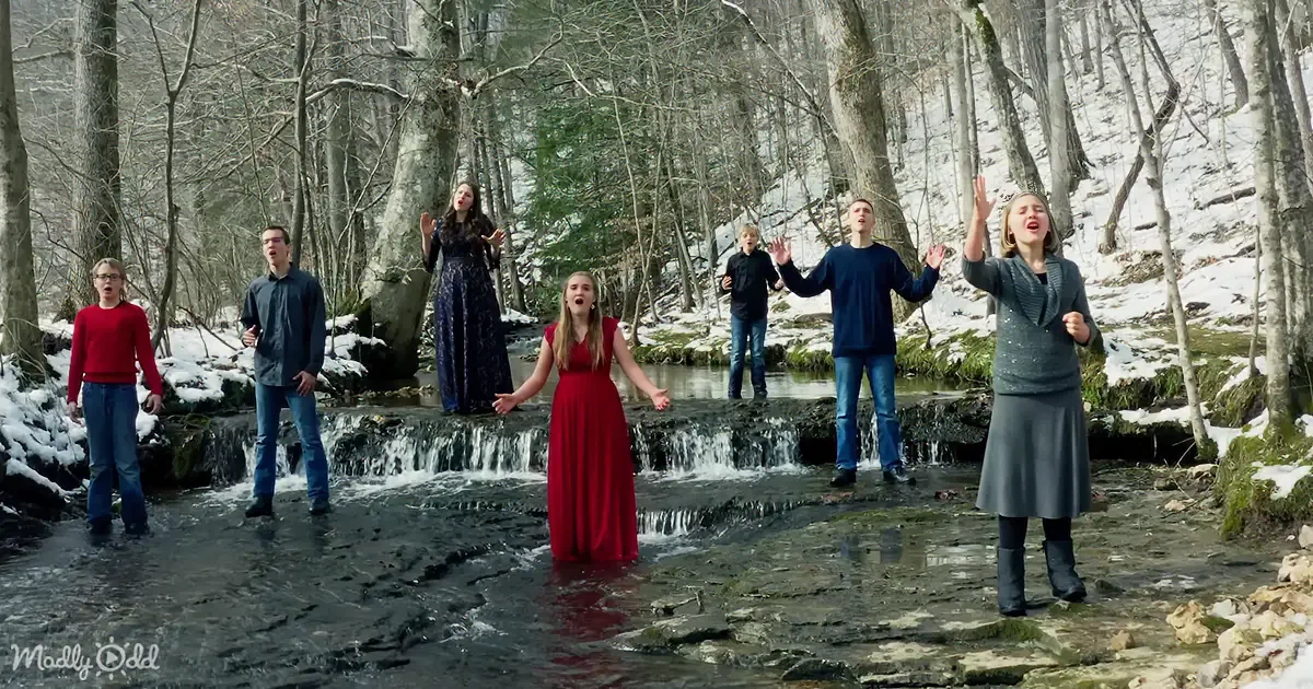 A group of people singing in a snowy forest near a small waterfall.