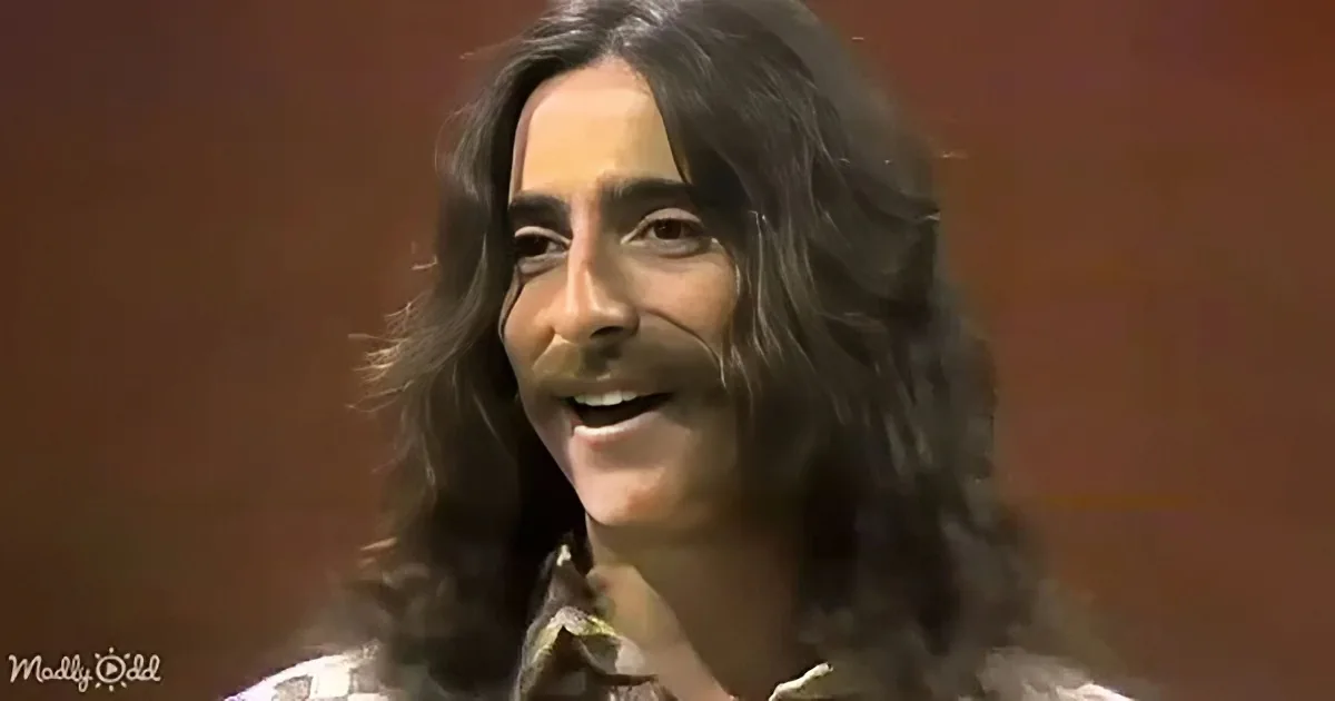 A person with long, dark hair and a checkered shirt is smiling and gesturing with their hand.