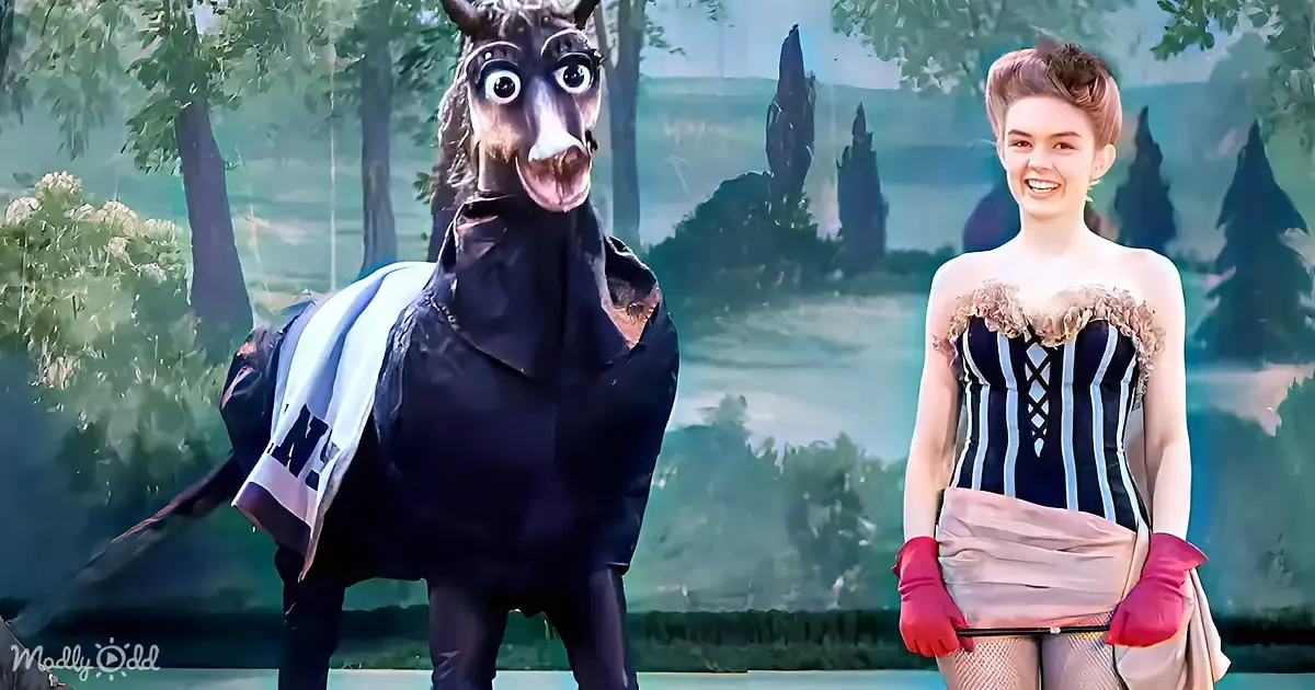 A person in a horse costume and another in a Victorian-style dress stand side by side against a forest backdrop.