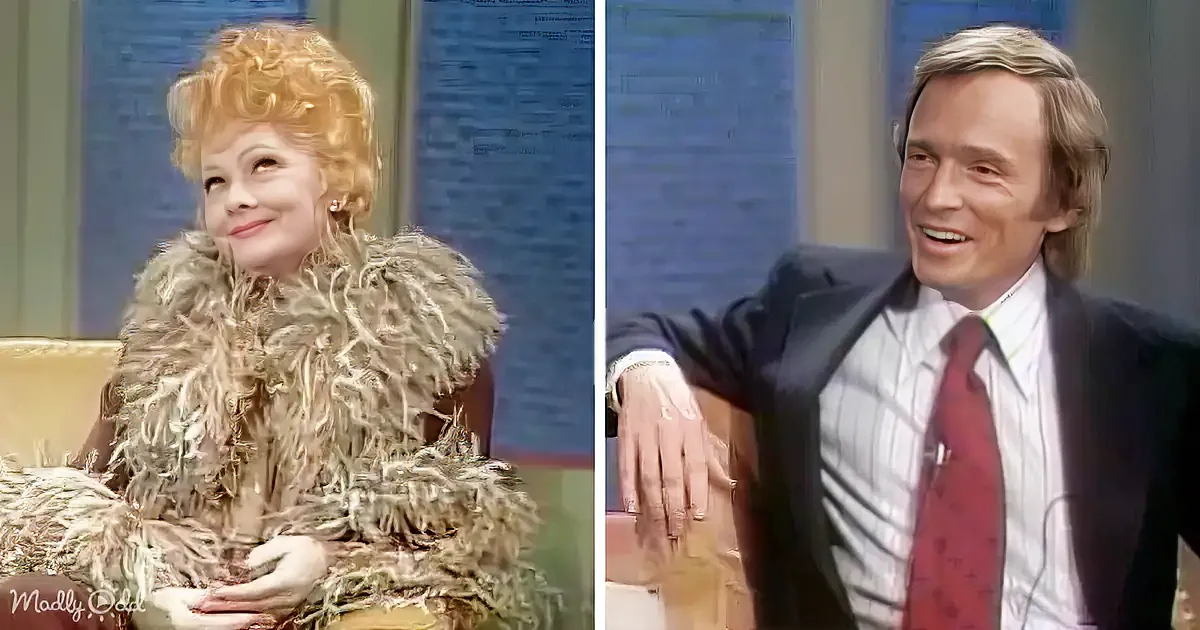 A woman in a fur coat and a man in a suit are seated, both smiling, on a talk show set.