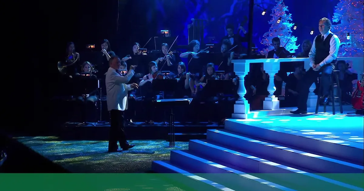 A man in a suit sings on stage with a band and Christmas tree in the background.