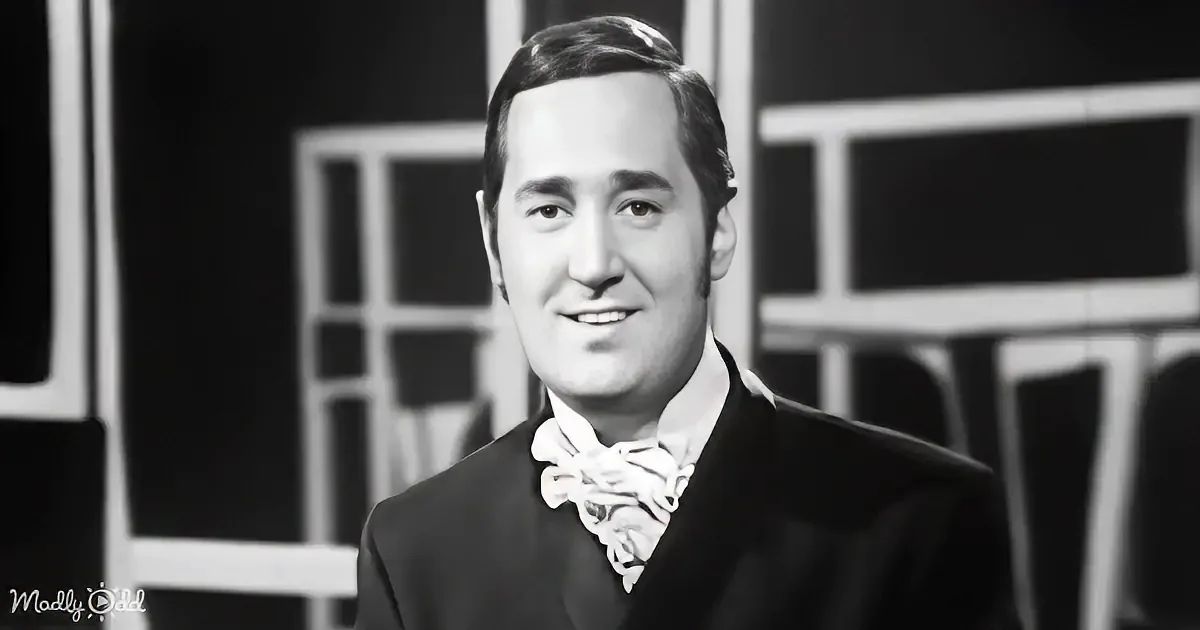 A man in a suit and bow tie smiles against a black-and-white background.