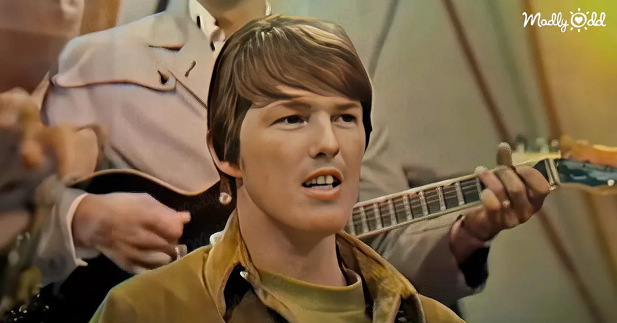 A man in a yellow jacket plays a guitar, singing passionately, with another person in the background.