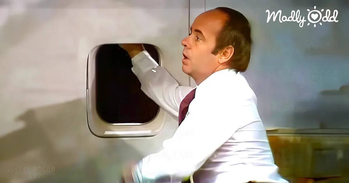 A man in a lab coat leans into a small window, appearing to be in a laboratory setting.