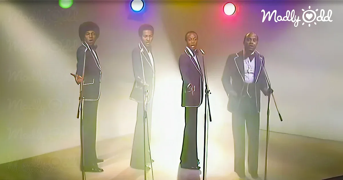 Four men in suits stand on stage with microphones, illuminated by colorful stage lights.