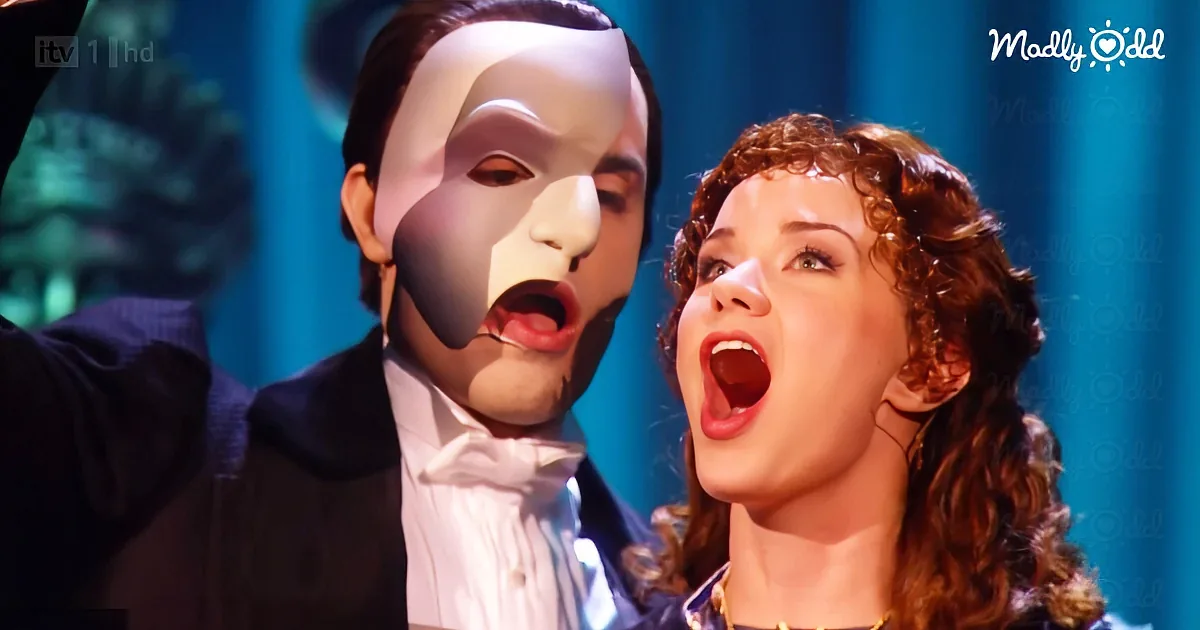 A man in a white mask and a woman with curly hair sing passionately on stage.