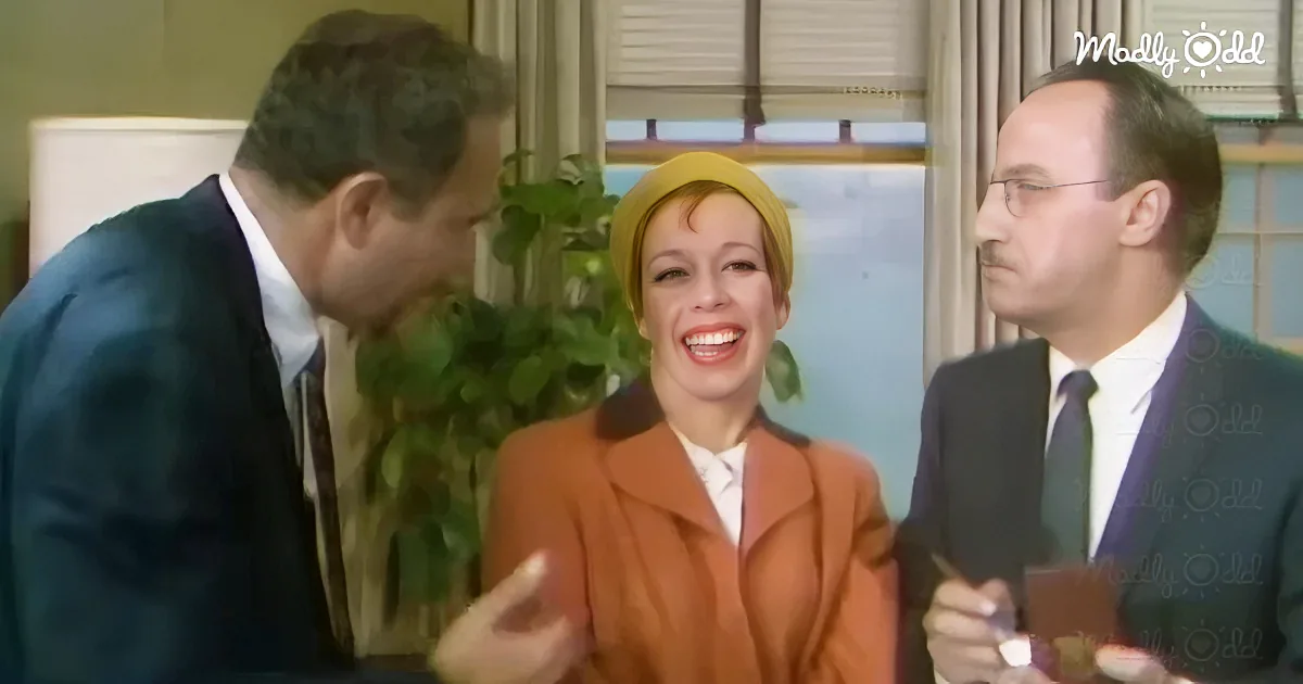 A woman in a yellow hat and orange coat laughs while two men in suits look on.
