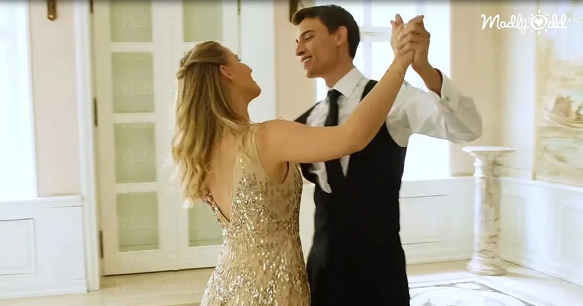 A couple in formal attire dances gracefully in a bright, elegant room.