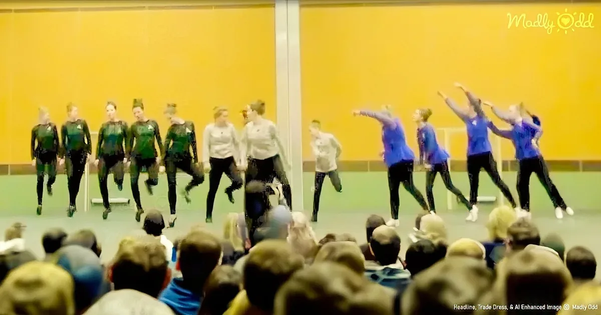 A group of dancers in green and blue outfits perform synchronized moves on a stage in front of an audience.