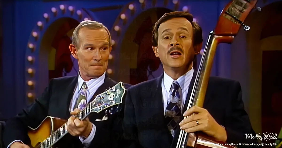 Two men in suits play guitar and bass on a stage with a colorful backdrop.